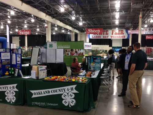 Photo of the Oakland County 4-H, MSU Extension, AgBioResearch and the College of Agriculture and Natural Resources booth. Several people standing and sitting and chatting.